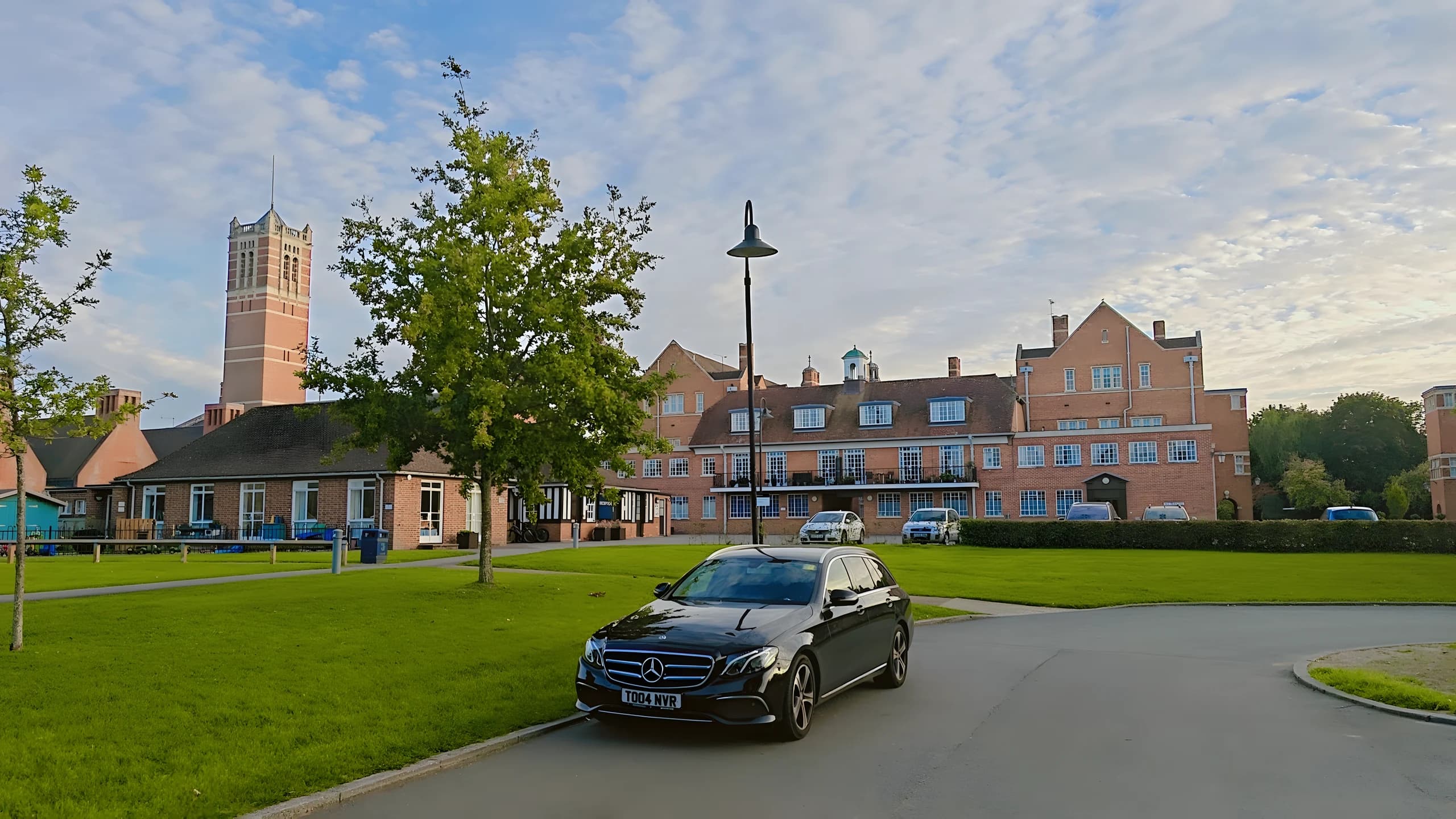 Black Mercedes estate car parked on a drive in front of red-brick buildings
